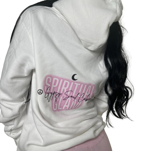 Close-up of a white oversized hoodie featuring colourful spiritual girl artwork, "Spiritual Glam" text in pink, peace symbols, and "Gypsy Soul Cabin" signature, worn by a woman with long black hair.