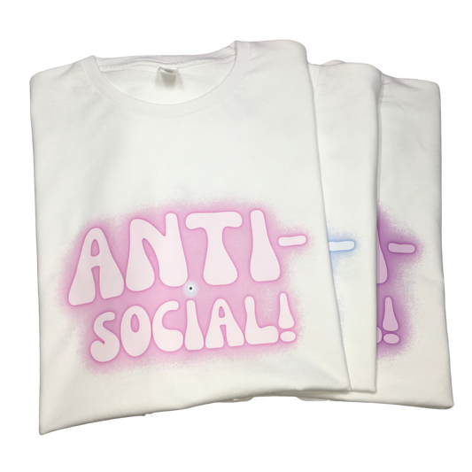 Three folded white T-shirts stacked, showing the Anti-Social slogan graphic and protective evil eye in different pink, blue, and purple spray-paint halo airbrush colour variants.
