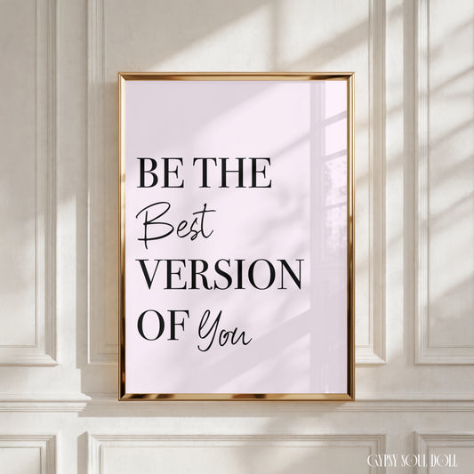 A framed typographic wall art print with the text 'BE THE Best VERSION OF You' in black lettering on a pale pink background, displayed against a white panelled wall with soft window shadows.