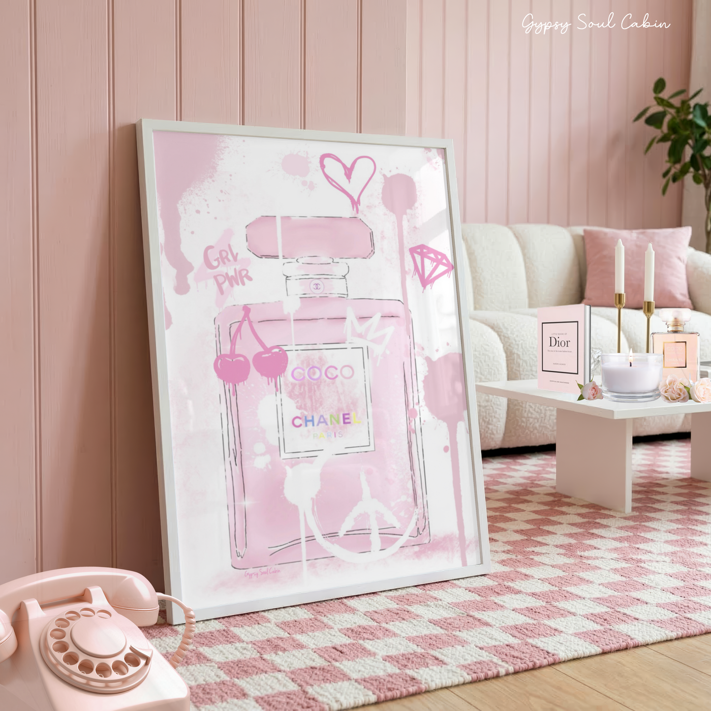 Glamorous pink Coco Chanel perfume bottle art print with graffiti drips, cherries, and a heart in a white frame on a pink checkered rug.