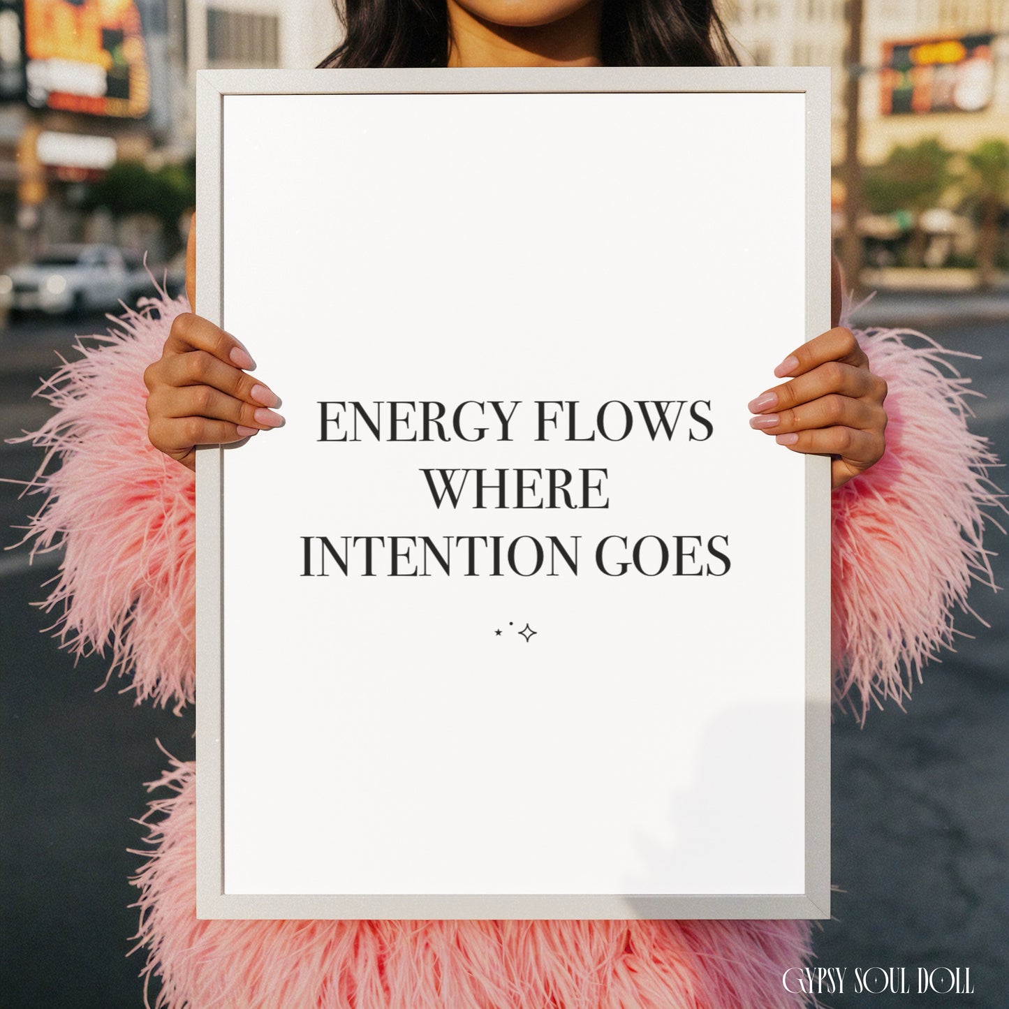 Minimalist black and white A4 typography print featuring the Law of Attraction quote Energy Flows Where Intention Goes, held by a woman in a pink fluffy coat.