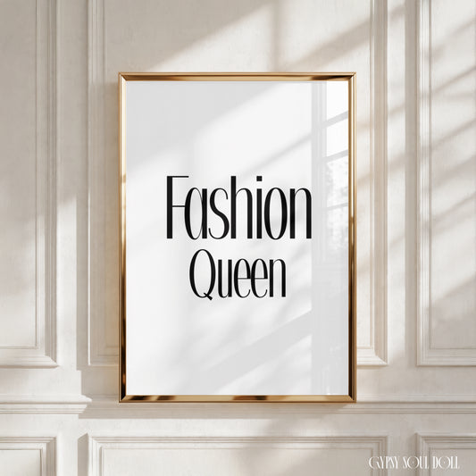 A framed typographic wall art print with the words 'Fashion Queen' in black serif text on a white background, set in a thin gold frame and leaning against a white paneled wall with soft window shadows.