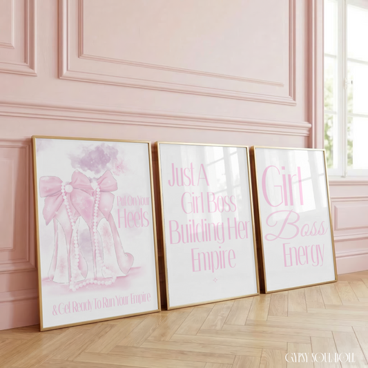 Set of three minimalist pink and white typography prints featuring a glamorous high heel illustration with pearls and empowering boss babe quotes, framed on a wooden floor against a pink panelled wall.
