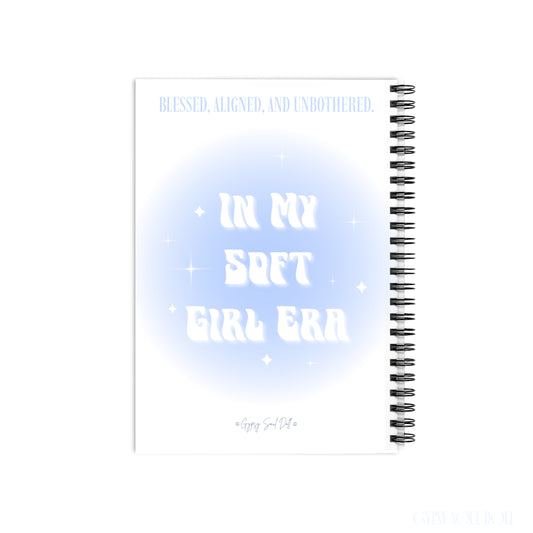 A white spiral notebook with a light blue and white graphic design on the cover. The cover features the text 'BLESSED, ALIGNED, UNBOTHERED and In My Soft Girl Era by Gypsy Soul Doll.