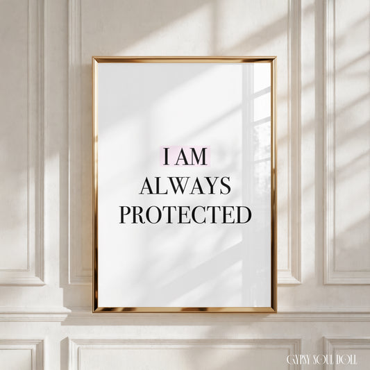 A framed typographic wall art print with the text 'I AM ALWAYS PROTECTED' in black serif lettering on a white background, set in a thin gold frame and displayed against a white paneled wall with soft window shadows.