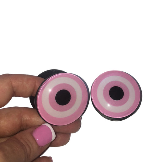 A close-up of a hand with pink French tip nails holding an expandable pastel pink and white glass-effect evil eye phone grip accessory.