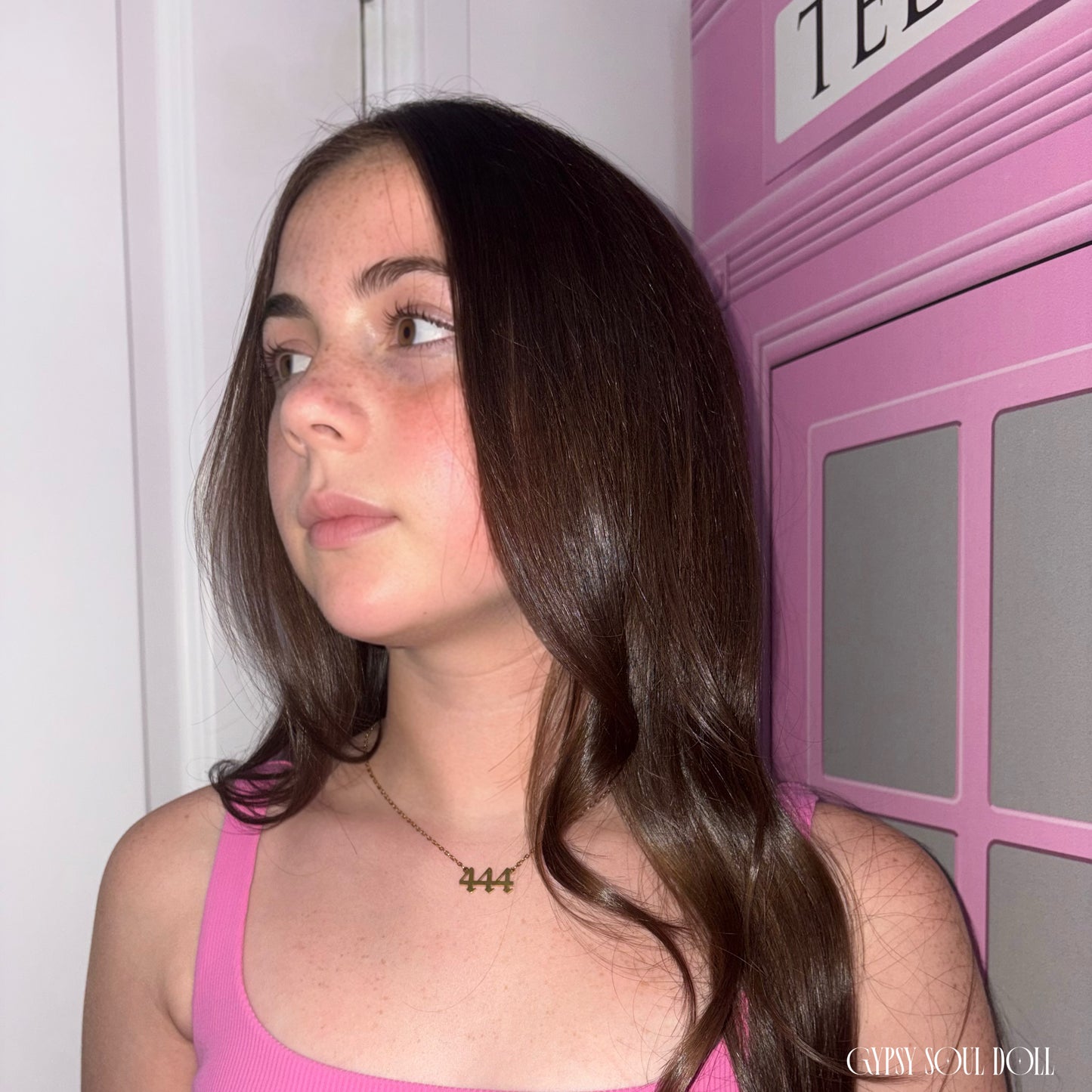 Model with long wavy brown hair looking to the side while wearing a bright pink top and the Gypsy Soul Doll dainty gold link chain necklace featuring a 444 angel number block charm.