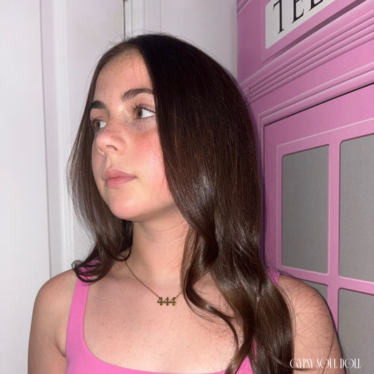 Model with long wavy brown hair looking to the side while wearing a bright pink top and the Gypsy Soul Doll dainty gold link chain necklace featuring a 444 angel number block charm.