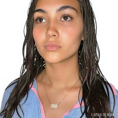 A close-up portrait of a model with wet dark hair wearing a delicate gold chain necklace with an 'angel numbers 888' pendant set against a plain white background.