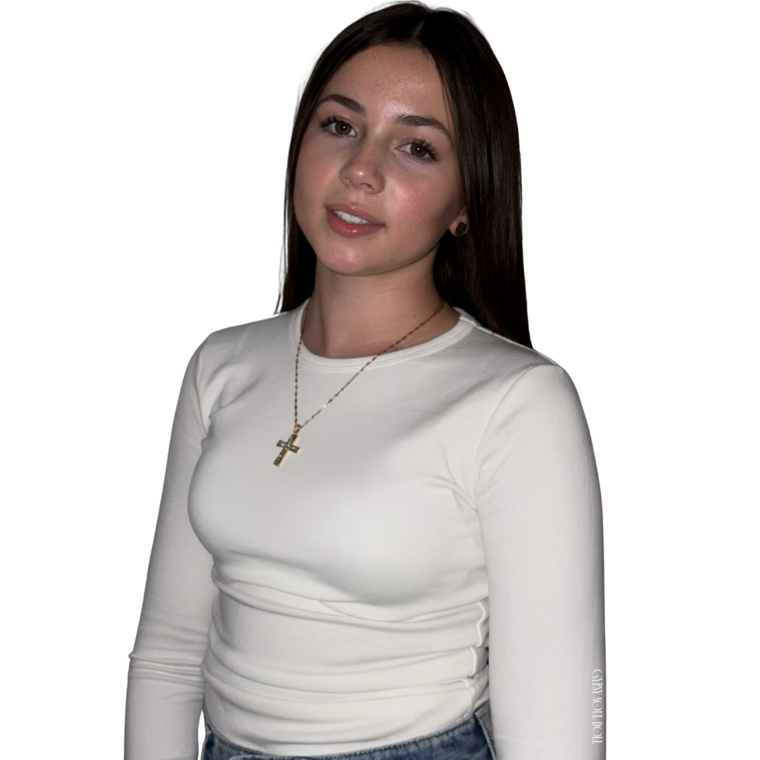 A model facing forward and smiling slightly against a white studio background, wearing a long-sleeved cream top accessorised with a polished gold link chain cross crucifix pendant necklace by Gypsy Soul Doll.
