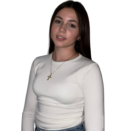 A model facing forward and smiling slightly against a white studio background, wearing a long-sleeved cream top accessorised with a polished gold link chain cross crucifix pendant necklace by Gypsy Soul Doll.