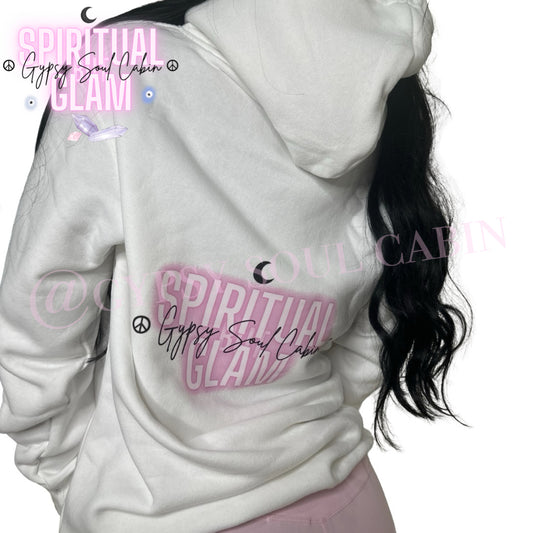 Close-up of a white oversized hoodie featuring colourful spiritual girl artwork, "Spiritual Glam" text in pink, peace symbols, and "Gypsy Soul Cabin" signature, worn by a woman with long black hair.