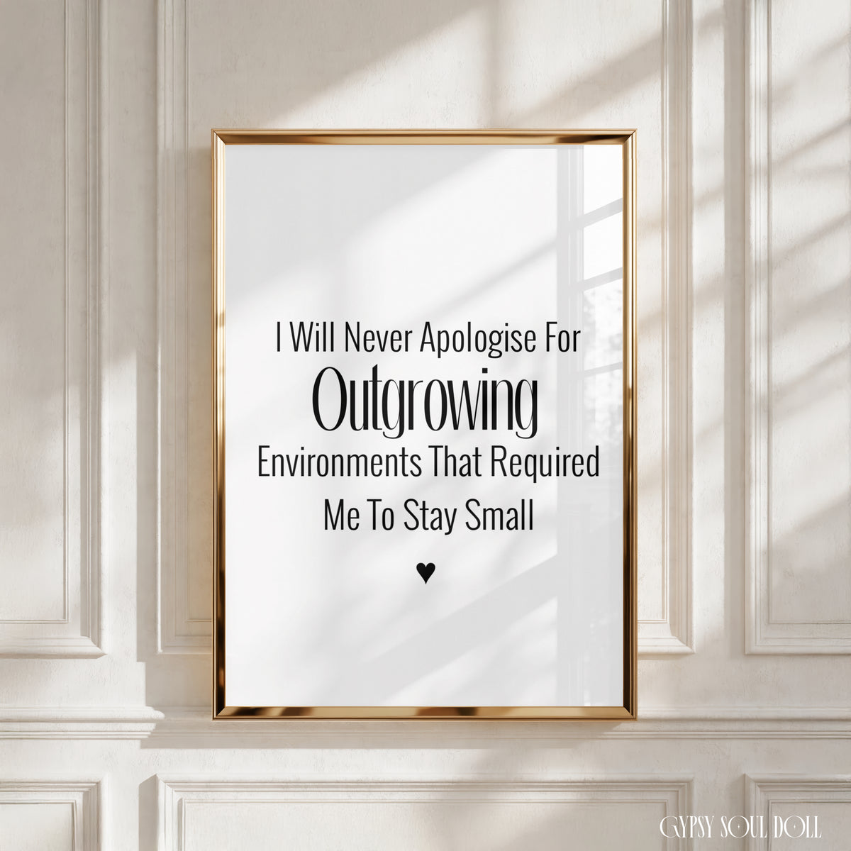 A framed typographic wall art print with black text on a white background, hanging on a cream panelled wall. The print reads, 'I Will Never Apologise For Outgrowing Environments That Required Me To Stay Small' with a small heart at the bottom by Gypsy Soul Doll.
