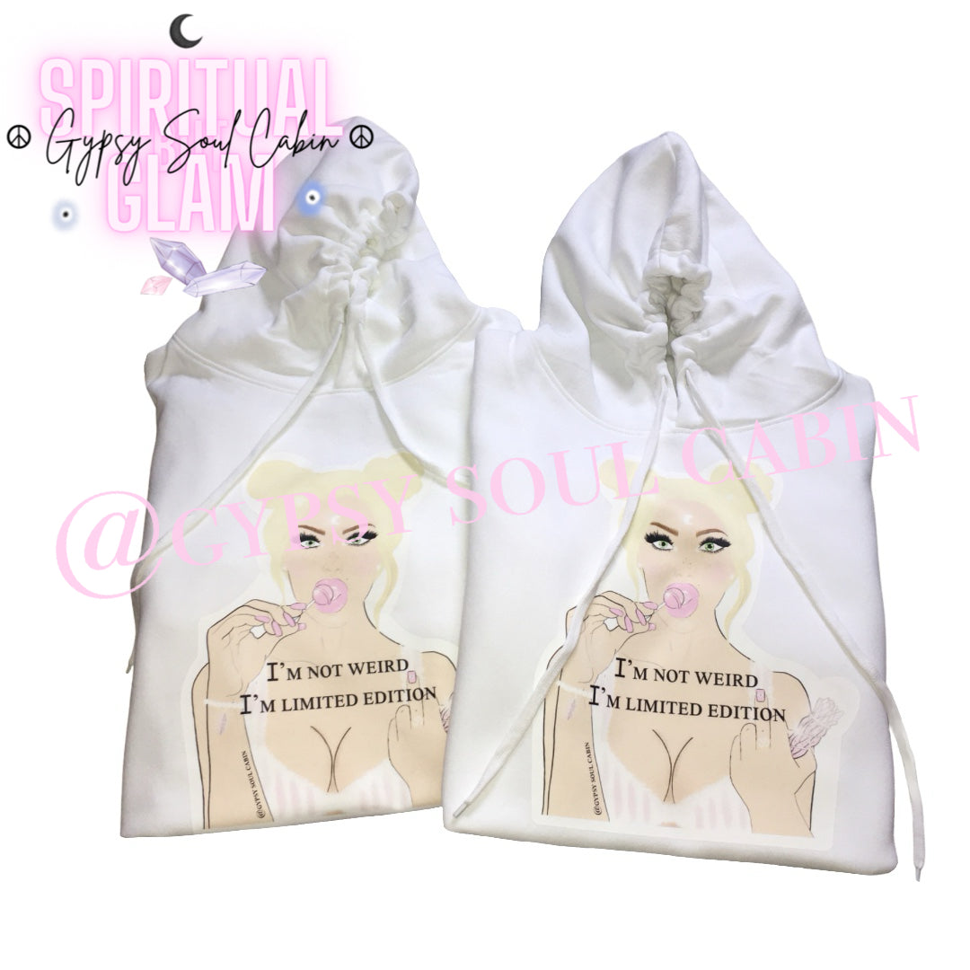 Two white oversized hoodies with a graphic of a woman with blonde hair, holding a lollipop, and the text "I'M NOT WEIRD, I'M LIMITED EDITION" printed on the front. The design features pastel colours and a playful, artistic style.