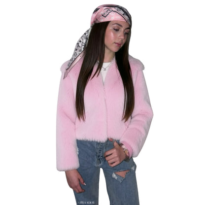 A woman modelling a light pink faux fur jacket, styled with a pink and black patterned monogram logo bandana, a white t-shirt, and distressed blue jeans against a plain white background.