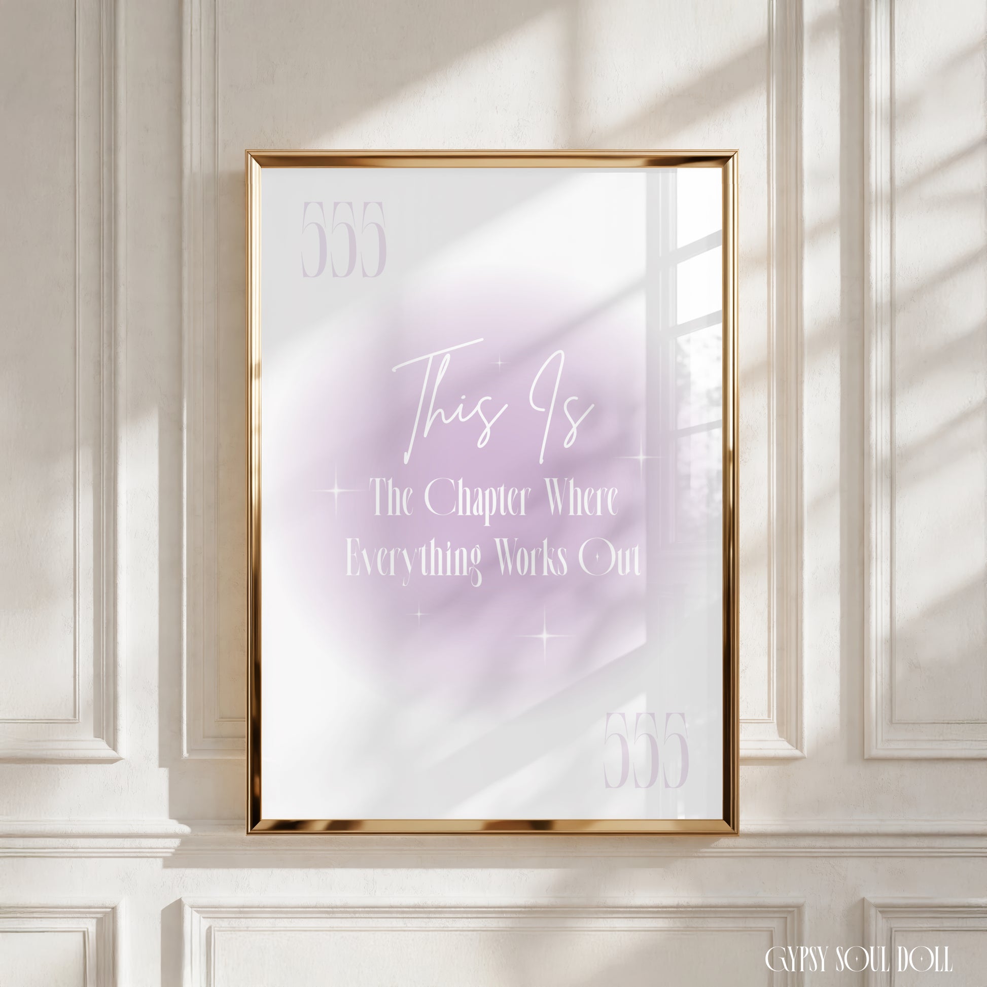 A framed motivational art print with the text 'This Is The Chapter Where Everything Works Out 555' in white script and serif fonts over a soft lavender and white gradient, displayed in a gold frame on a white paneled wall with realistic window shadow light casting across the scene.