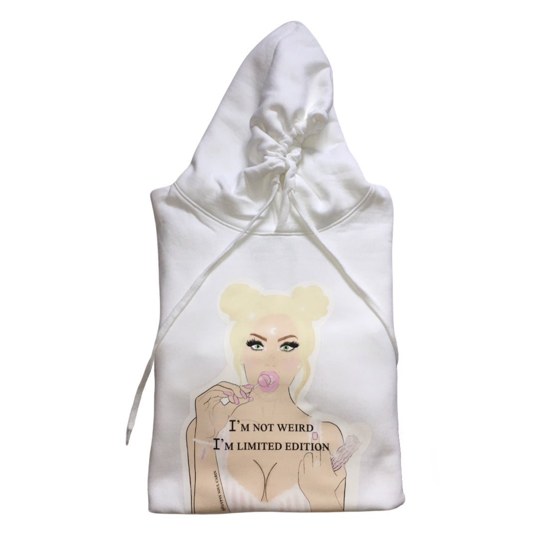 A white oversized hoodies with a graphic of a woman with blonde hair, holding a lollipop, and the text "I'M NOT WEIRD, I'M LIMITED EDITION" printed on the front. The design features pastel colours and a playful, artistic style.