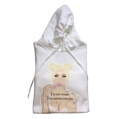A white oversized hoodies with a graphic of a woman with blonde hair, holding a lollipop, and the text "I'M NOT WEIRD, I'M LIMITED EDITION" printed on the front. The design features pastel colours and a playful, artistic style.