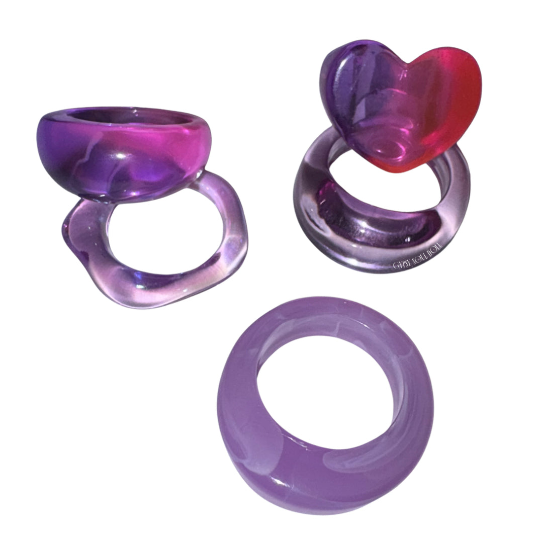 Overhead view of the Grape Soda candy acrylic ring stack featuring four retro purple resin rings including a vibrant ombre heart ring and wavy translucent bands.