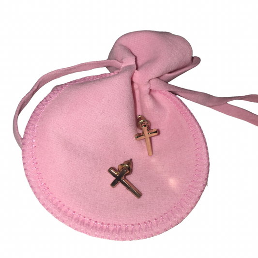 Two small gold-toned cross-shaped stud earrings displayed on a round pink drawstring pouch against a white background.
