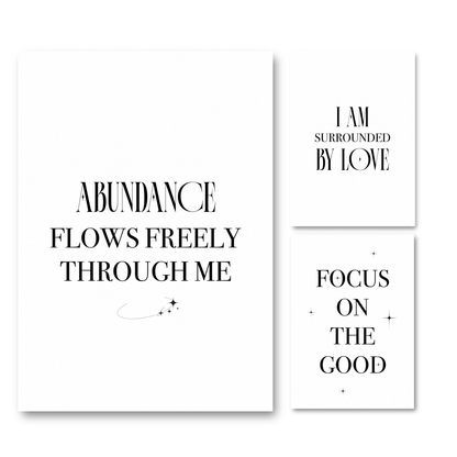 Three minimalist white art prints with black typography on a white background. The largest print reads 'ABUNDANCE FLOWS FREELY THROUGH ME' with a small curved line and star motif.