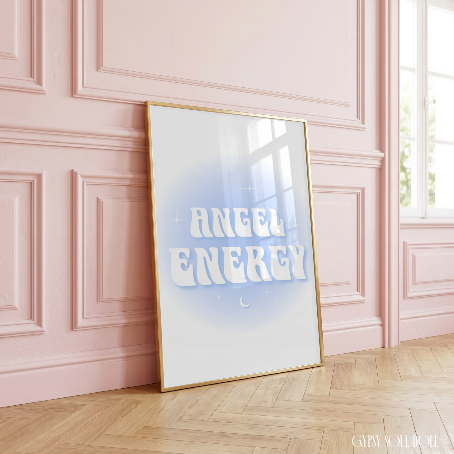 Angel Energy typography print featuring wavy retro white lettering with a tiny crescent moon and stars on a soft blue aura gradient background, styled in a luxury gold frame leaning against a pastel pink wall.