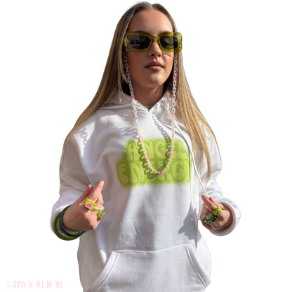 A woman modelling a white hoodie with a bright lime green 'ANGEL ENERGY' graphic on the chest, styled with neon green sunglasses, a chain lanyard, matching wrist accessories and chunky Y2K fashion rings against a plain white background.