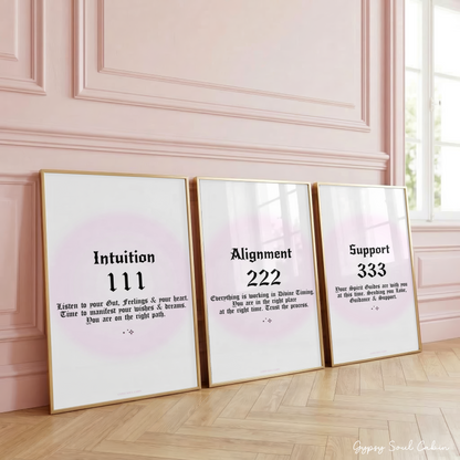 Set of three minimalist manifestation wall art prints featuring angel numbers 111, 222, and 333 in bold black gothic typography over a soft pastel pink aura gradient backdrop, framed on a wooden floor against a pink panelled wall.