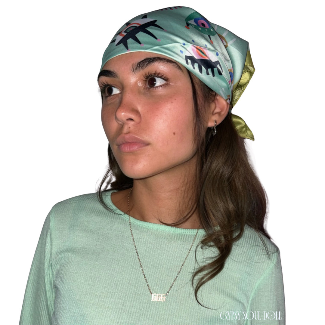 A model wearing a green evil eye silk boho headscarf paired with a matching mint green ribbed long-sleeve top and an Angel number 666 gold necklace.