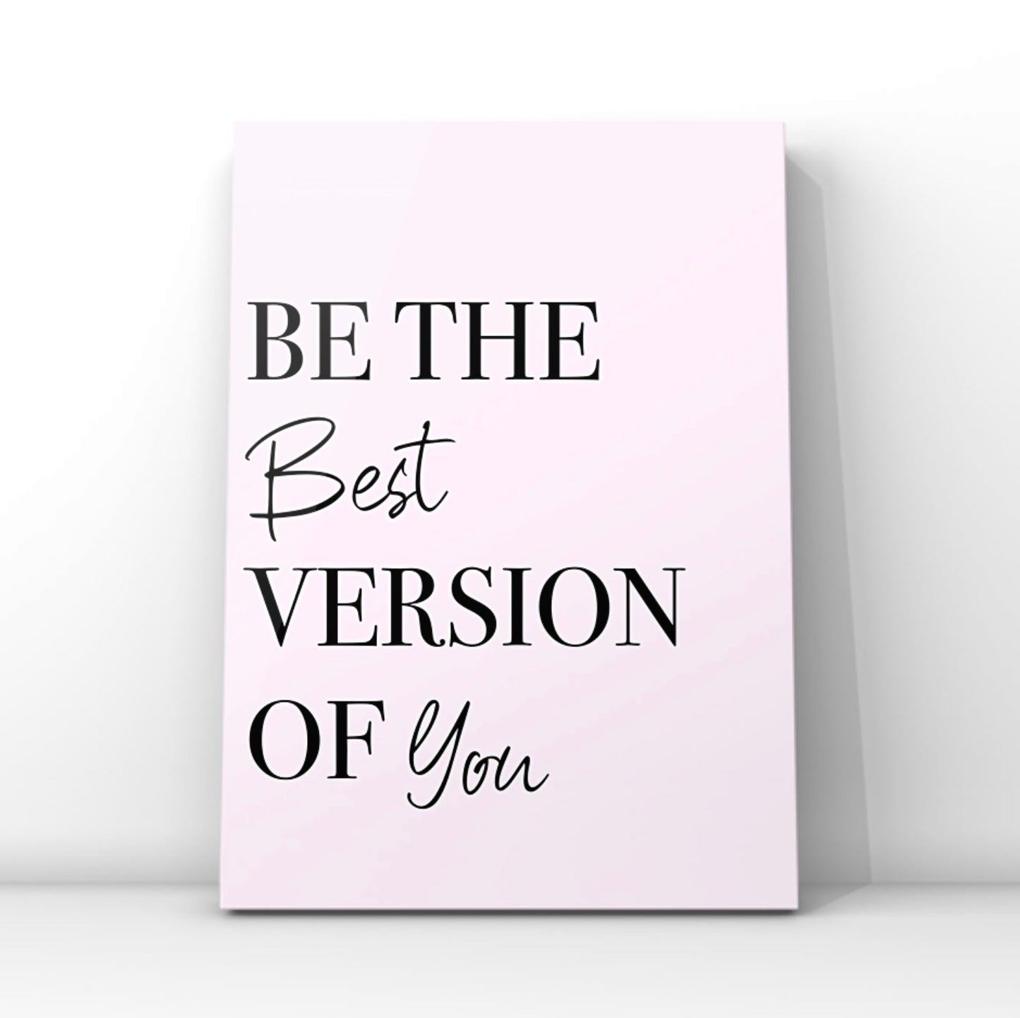 Minimalist pink affirmation print reading Be The Best Version Of You in a combination of crisp black serif and cursive script fonts, leaning against a clean white wall backdrop.