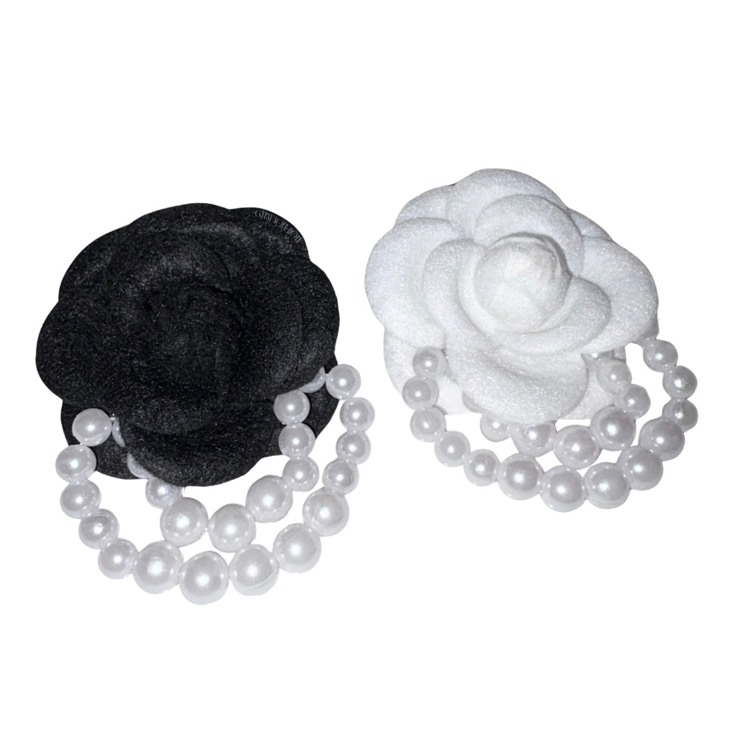 Front view showcasing a monochrome pair of camellia fabric flower brooch pins in velvet black and frosted white, featuring double draped faux pearl bead strands looping below the petals.