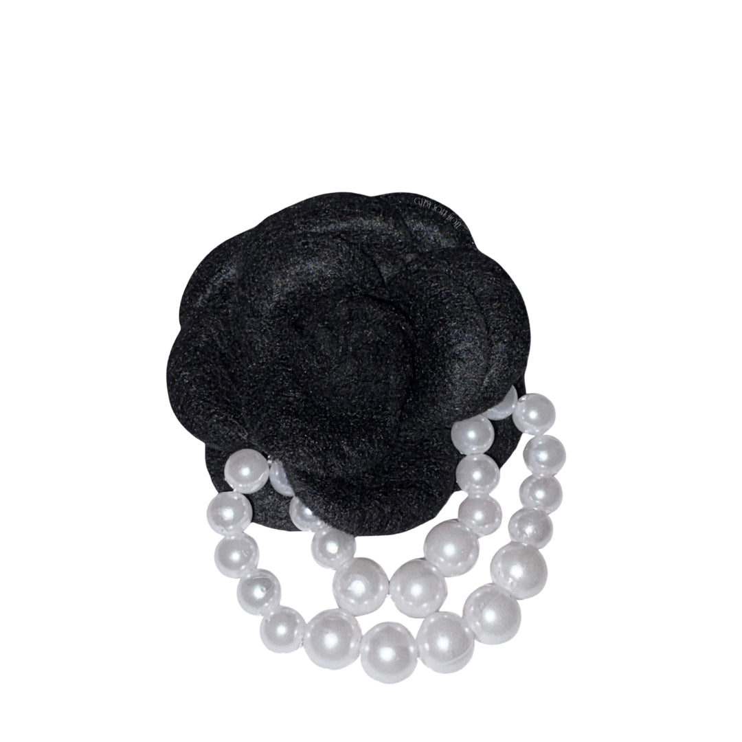 Close-up front view of the deep black velvet camellia flower brooch pin decorated with two elegant draped strands of white faux pearl beads.