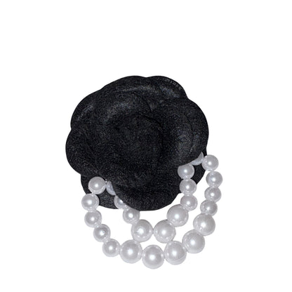 Close-up front view of the deep black velvet camellia flower brooch pin decorated with two elegant draped strands of white faux pearl beads.