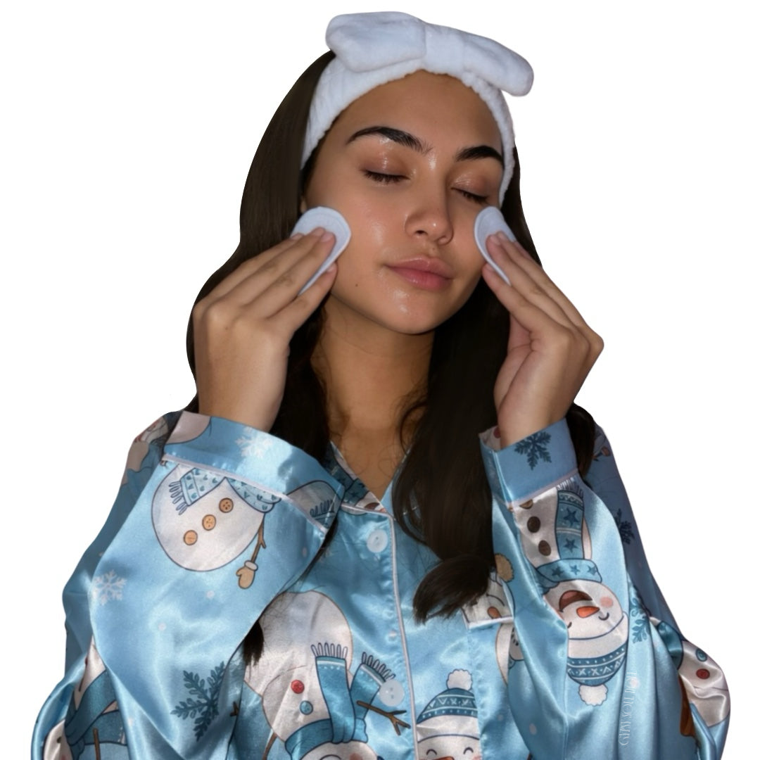 A woman wearing a light blue and white pyjama top with a snowman print and a white headband, using circular cleansing flannel pads on her face against a plain white background by Gypsy Soul Doll.