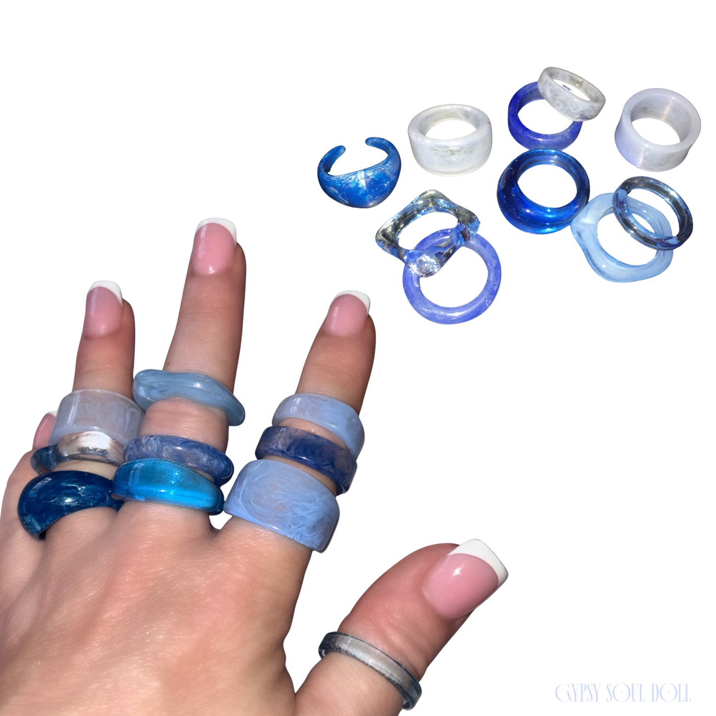 A hand wearing multiple chunky resin rings in shades of blue, navy, and translucent white, with additional rings displayed on a plain white background. The brand name 'GYPSY SOLID DOLL' is visible in the bottom right corner.