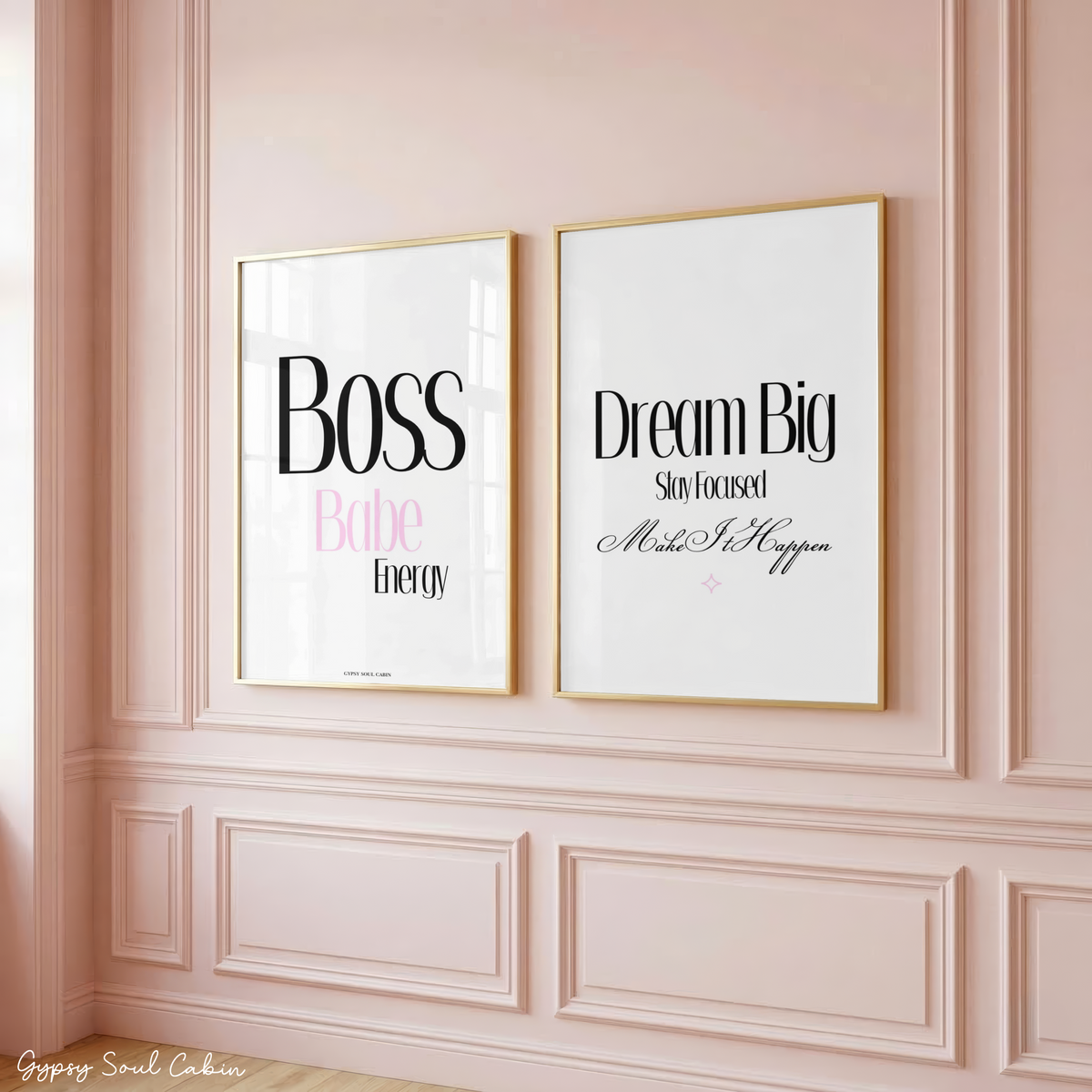 Two minimalist typography prints reading "Boss Babe Energy" and "Dream Big Stay Focused Make It Happen" in gold frames, hanging on a classic panelled pink wall.