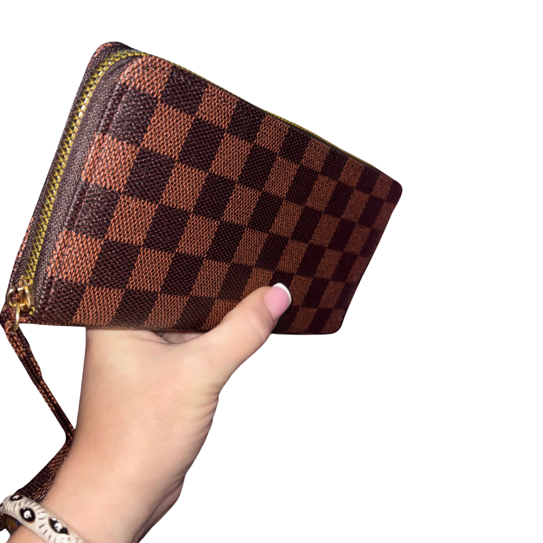 A hand holding a brown and dark brown checkerboard monogram zip-around wallet with a wrist strap, shown against a plain white background.