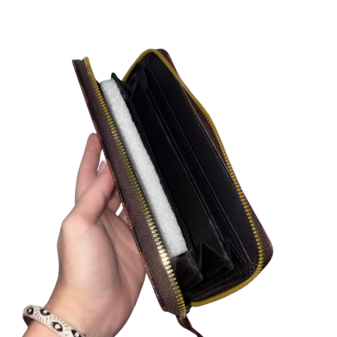 A hand holding an open brown and black zip-around wallet with gold-toned zippers and a black interior card slots, against a plain white background.