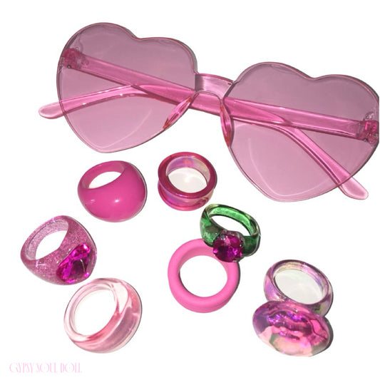 Flat lay view of the Gypsy Soul Doll Candy Crush festival combo, featuring oversized translucent pink heart fashion glasses resting above an assorted scattered collection of chunky pink, clear glitter, and green resin bubble rings.