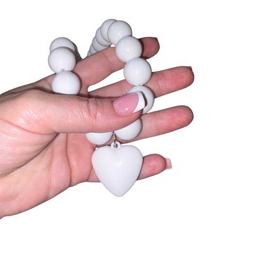 A white beaded necklace with a white heart-shaped pendant, held in a hand against a plain white background.