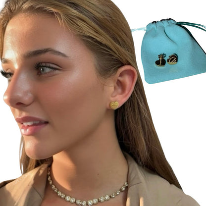 A side profile view of a young woman wearing small gold heart-shaped stud earrings and a gold bezel tennis necklace, pictured next to a turquoise blue drawstring pouch containing a pair of silver heart studs.