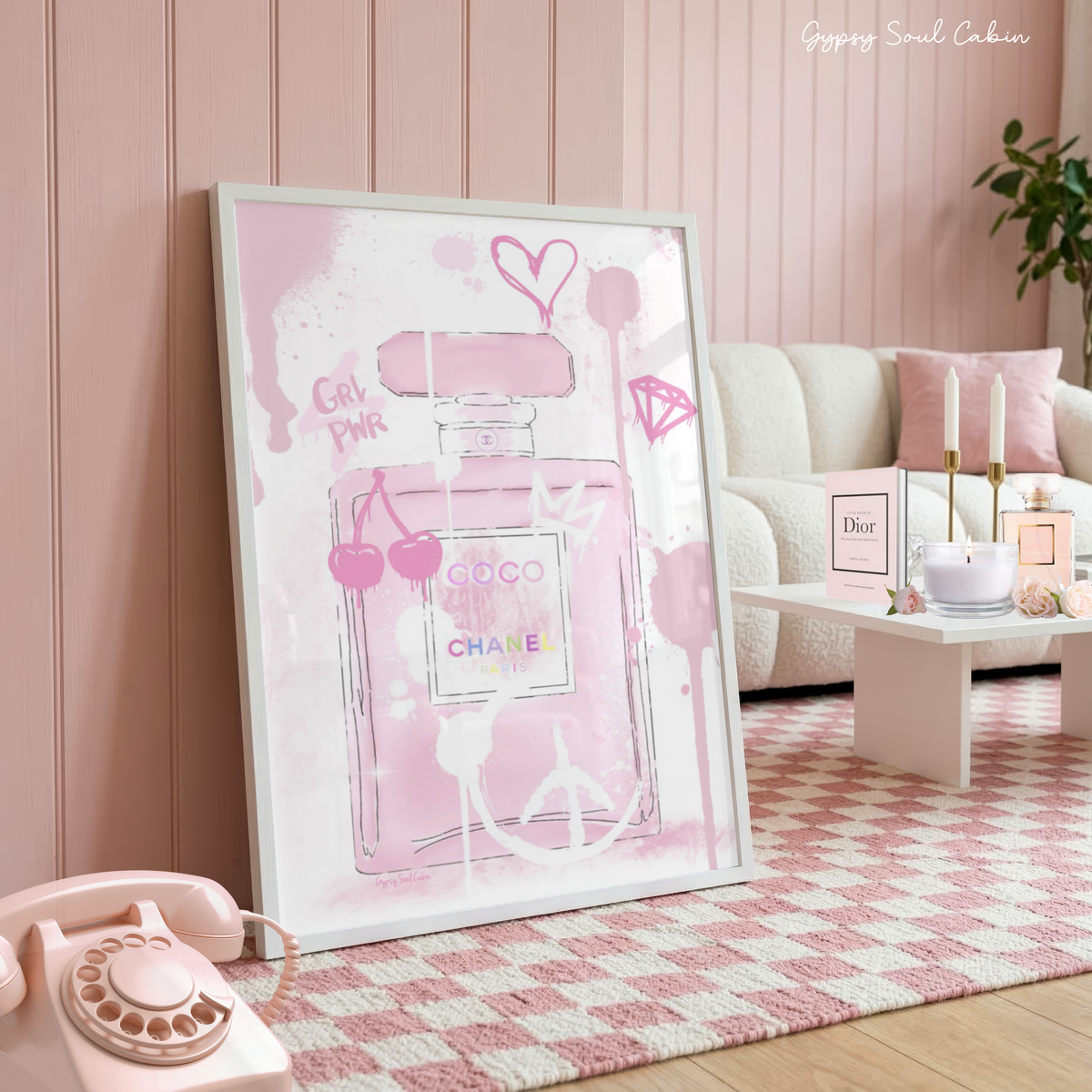 Glamorous pink Coco Chanel perfume bottle art print with graffiti drips, cherries, and a heart in a white frame on a pink checkered rug.