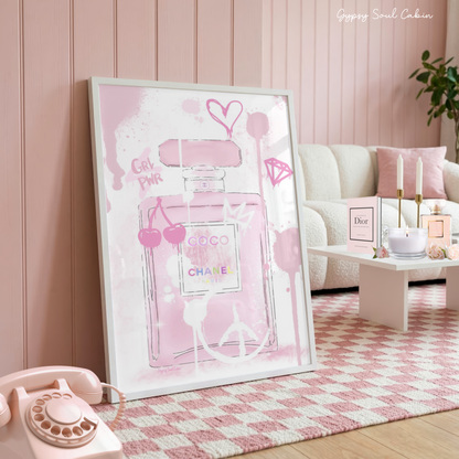 Glamorous pink Coco Chanel perfume bottle art print with graffiti drips, cherries, and a heart in a white frame on a pink checkered rug.