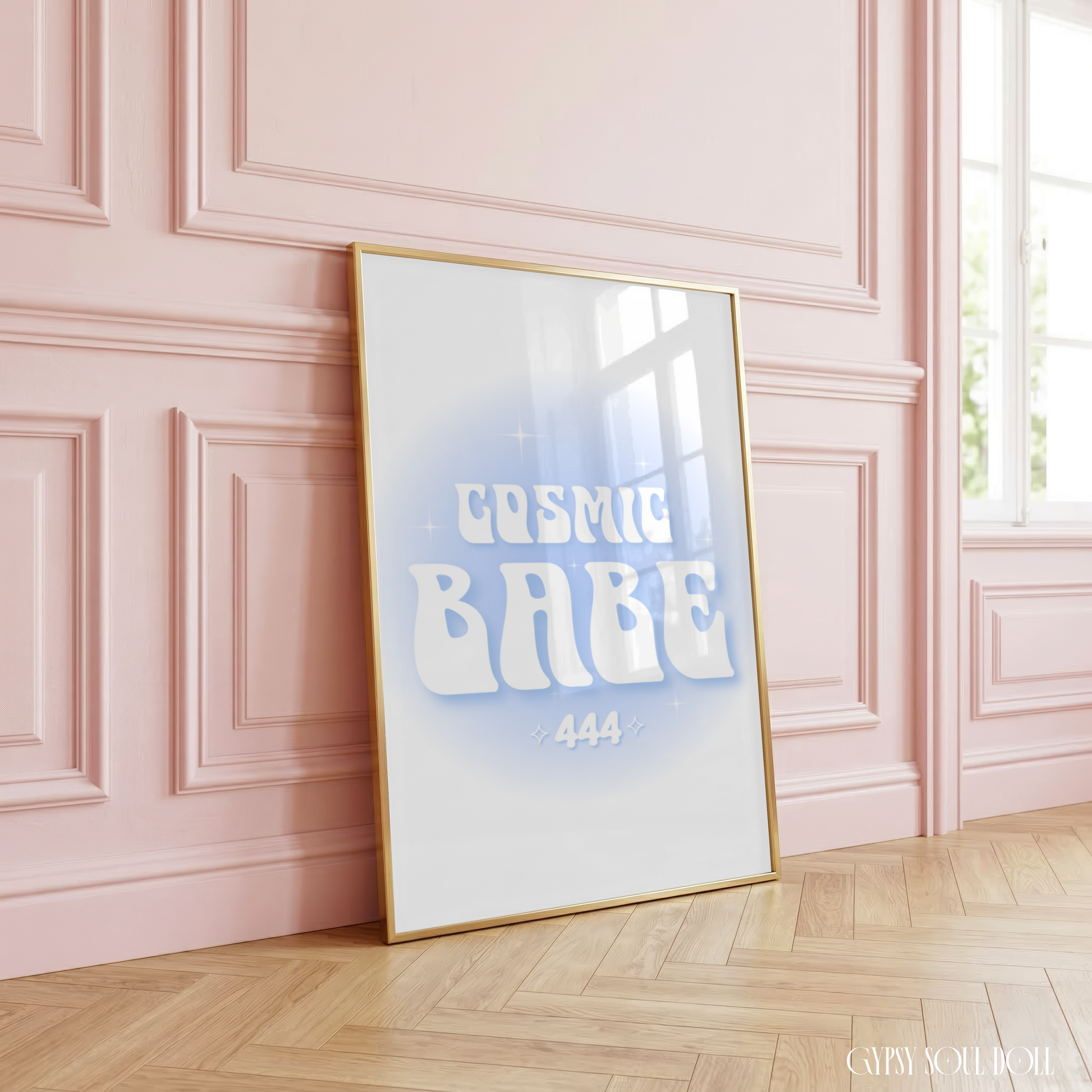 Cosmic Babe typography print featuring a retro white font with a 444 angel number and soft blue aura gradient background, beautifully styled in a luxury gold frame, leaning against a pastel pink panelled wall.