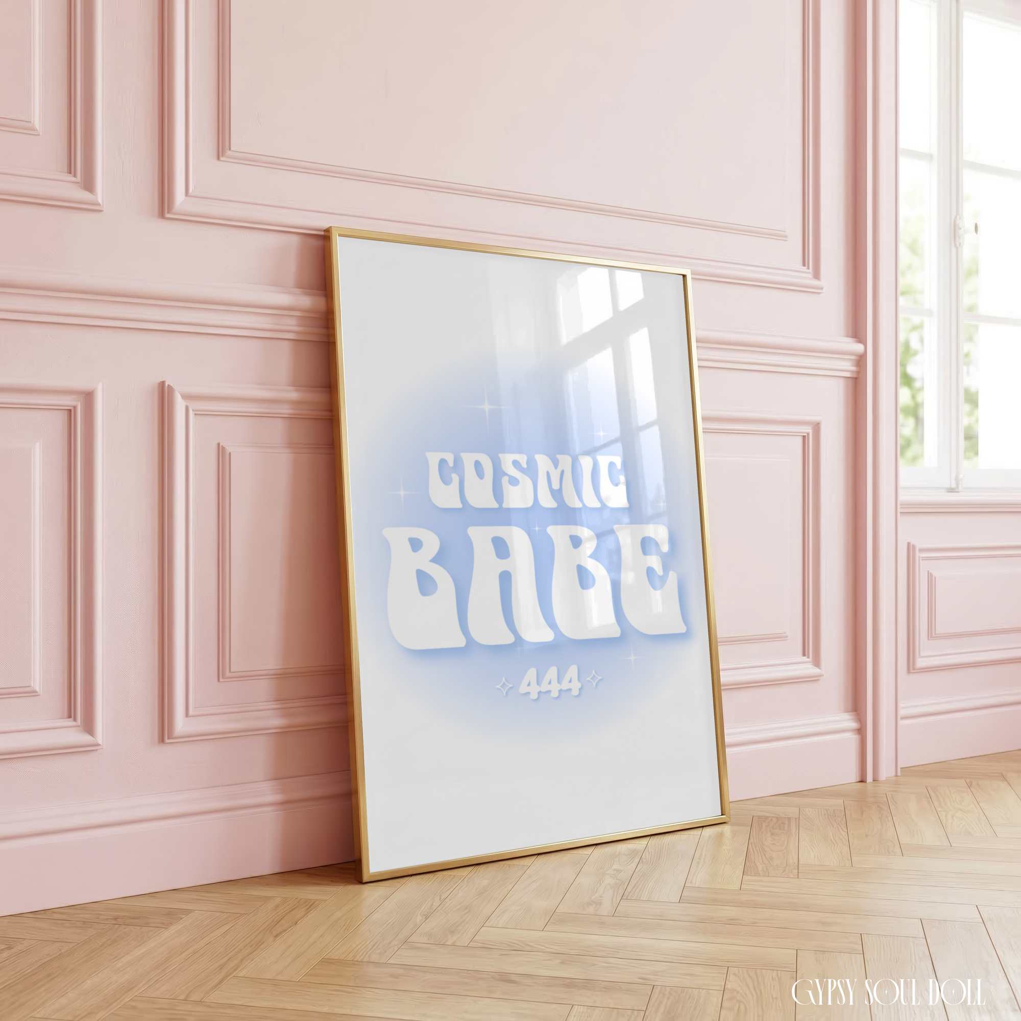 Cosmic Babe typography print featuring a retro white font with a 444 angel number and soft blue aura gradient background, beautifully styled in a luxury gold frame, leaning against a pastel pink panelled wall.