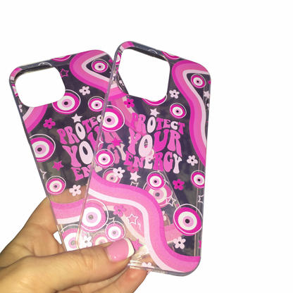 A close-up view of a hand with a pink French manicure holding up two clear Gypsy Soul Doll phone cases printed with groovy pink evil eyes, retro waves, and the pink bubble text slogan "Protect Your Energy.”