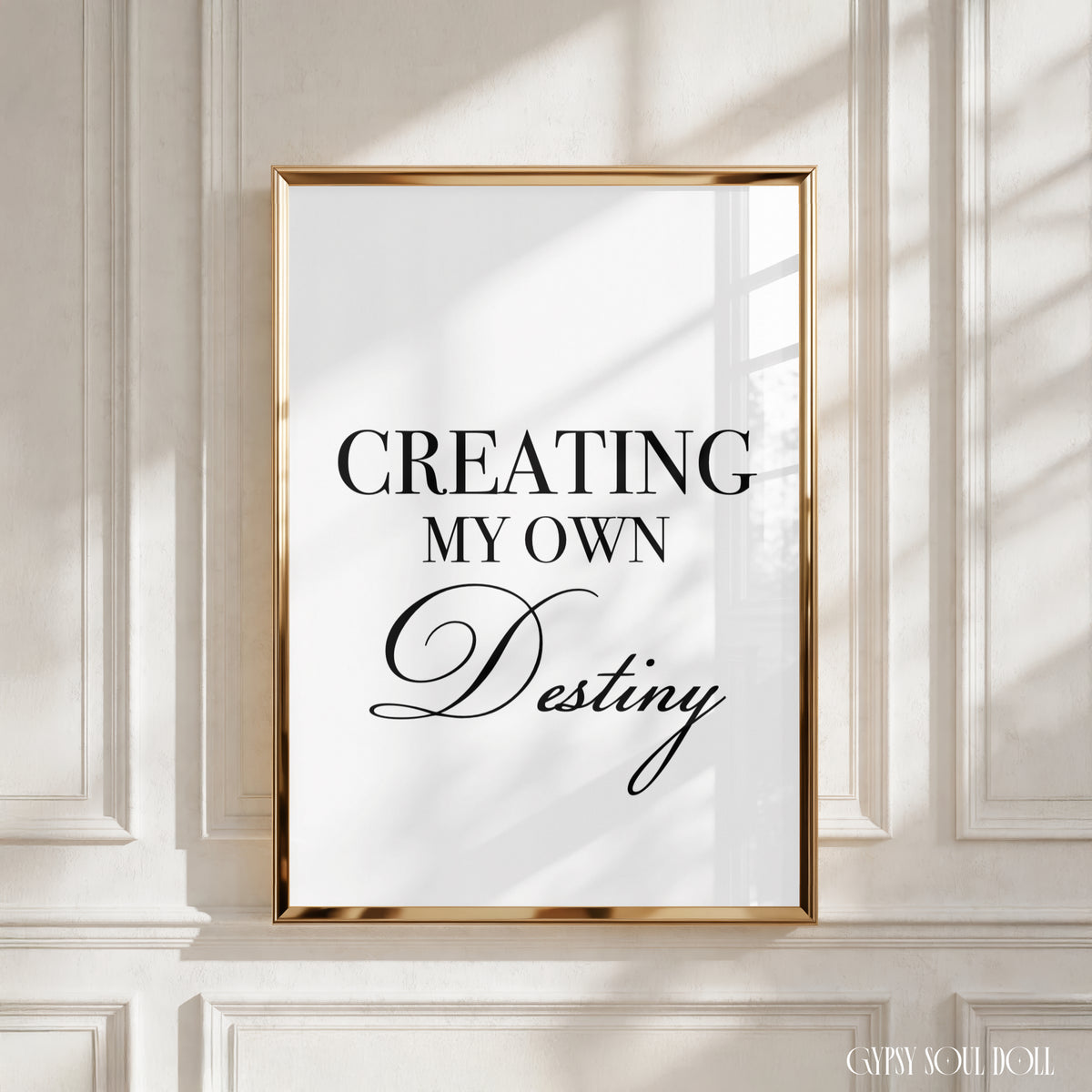 A framed typographic wall art print with the text 'CREATING MY OWN Destiny' in black lettering on a white background, mounted against a cream panelled wall with soft window shadows by Gypsy Soul Doll.