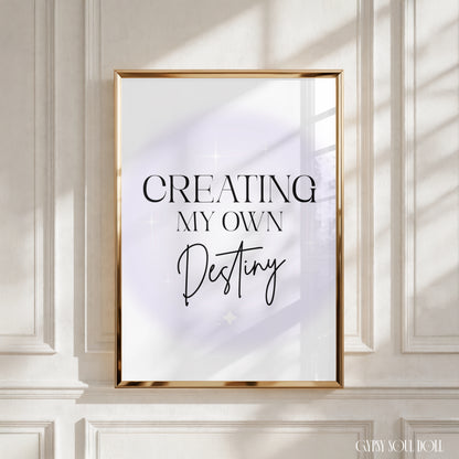 A framed typographic wall art print hanging on a white panelled wall. The print reads “CREATING MY OWN Destiny” in black serif and script text over a soft white and pale lavender background by Gypsy Soul Doll.