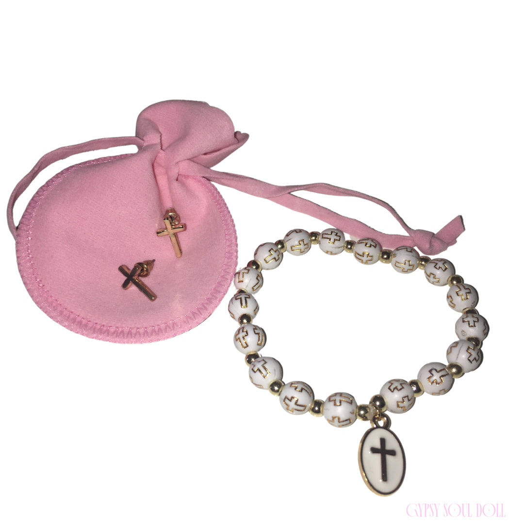 A white beaded bracelet with gold crosses and a white oval cross charm, shown next to a small pink drawstring pouch containing two small gold plated cross stud earrings on a white background.