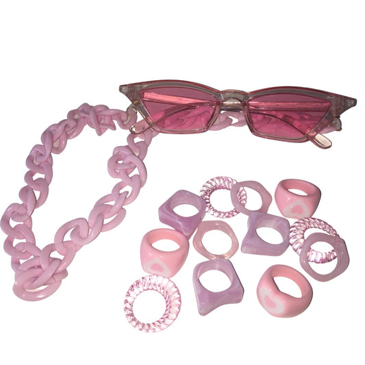 Flat lay view of the Gypsy Soul Doll Cyber Candy festival combo, featuring translucent pink cat-eye fashion glasses with a thick pink acrylic link chain lanyard next to a scattered assortment of pink resin heart rings, geometric bands, and clear spiral rings.